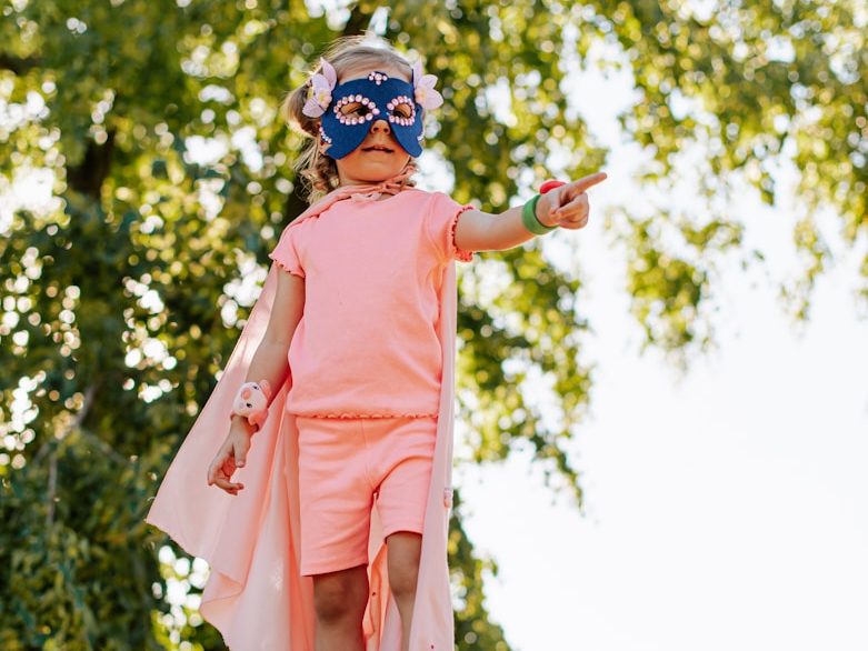 Starke Kids Ein kleines Kind in einem Superhelden-Kostüm zeigt entschlossen auf etwas.