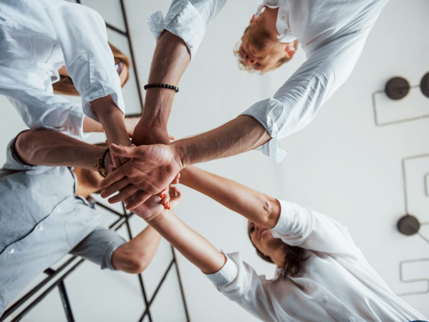 Starke Teams Vier Hände in einem Kreis, die sich aufeinanderlegen, symbolisieren Teamarbeit.